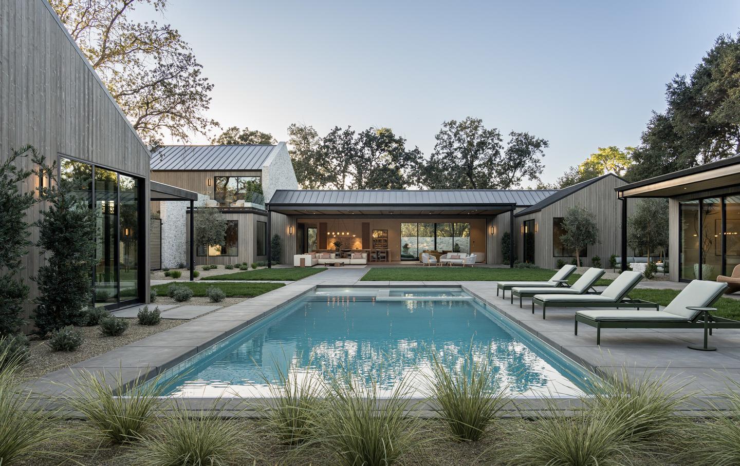 A courtyard with a pool and lounge chairs is surrounded by a modern home with large glass doors and windows. 