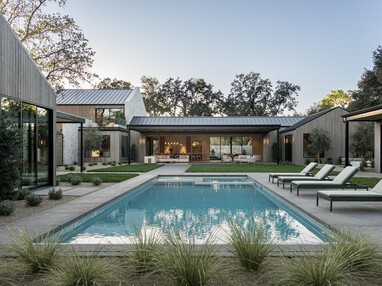 A courtyard with a pool and lounge chairs is surrounded by a modern home with large glass doors and windows. 