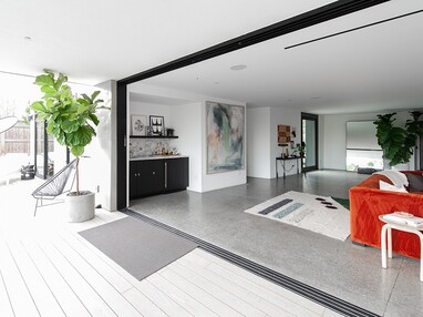 A living room with floor-to-ceiling, pocketing multi-slide doors open wide to the backyard patio.