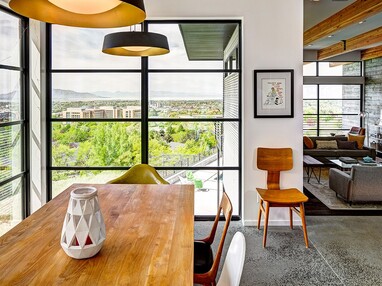 Large, divided lights fixed windows frame views of green landscape around a dining room table.