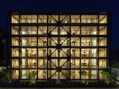 A nighttime view of the multi-family building with walls of glass on every floor.