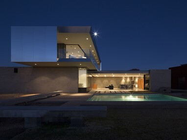 A view of the two-story, concrete and glass home that completely opens to the landscape through wall-to-ceiling multi-slide doors.