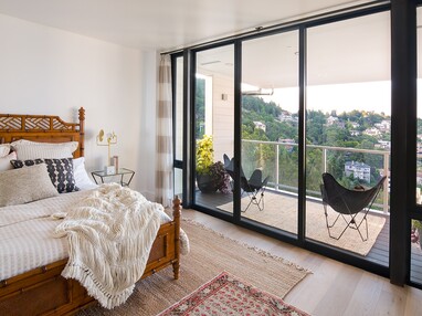 A large sliding glass door connects this bedroom to a balcony overlooking the green neighborhood below.