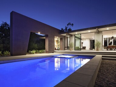 A home with a large pool opens up through sliding glass doors.