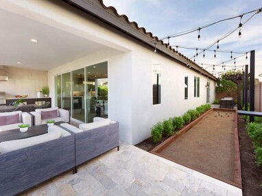 A view of an outdoor living area and bocce ball playing space separated from the indoors by a closed multi-slide glass door.