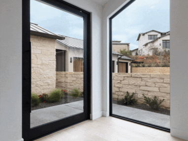 A massive pivot door, mirrored by a fixed window, provides a seamless indoor-outdoor connection.
