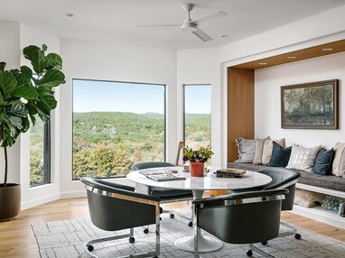 Natural daylight pours into a combined dining and den area through a picture window flanked by fenestration.