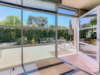 The massive hinged-door and accompanying wall of windows opens to a back patio surrounded by shrubbery.