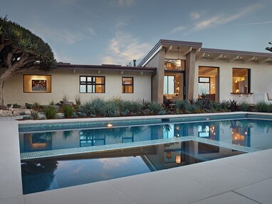 A view of the back of the home, dotted with windows and a large glass door, and a large swimming pool.