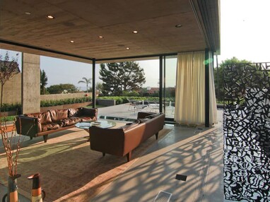 The stunning sunroom with two brown leather couches around a glass table is surrounded on three sides by immense moving panels of glass.