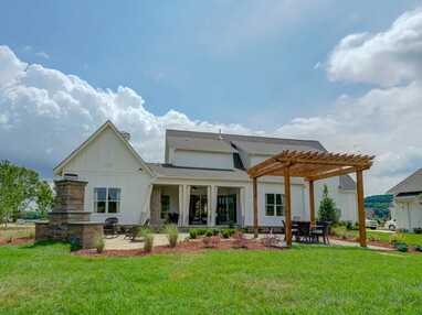 A lush backyard with green grass and a tall pergola is connected to the back of a house with multi-slide glass doors.