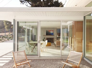 A mid-century modern home features a glass wall with a sliding glass door.