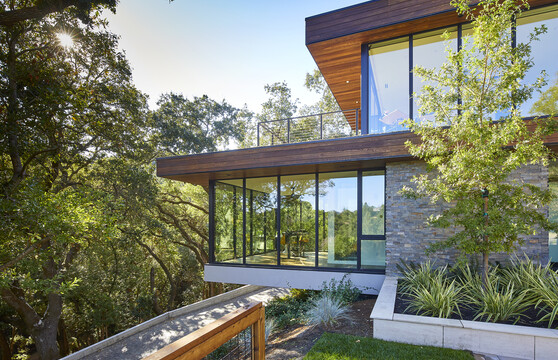 Two stories of a modern home with entirely glass walls reflect the trees across the driveway.