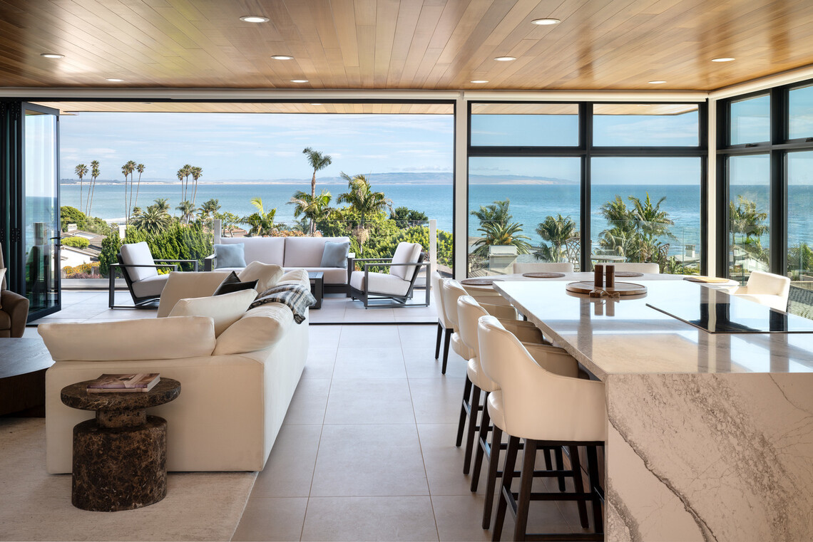 Open-concept living and dining space in a Pismo Beach residence with a wide glass opening overlooking the Pacific Ocean.