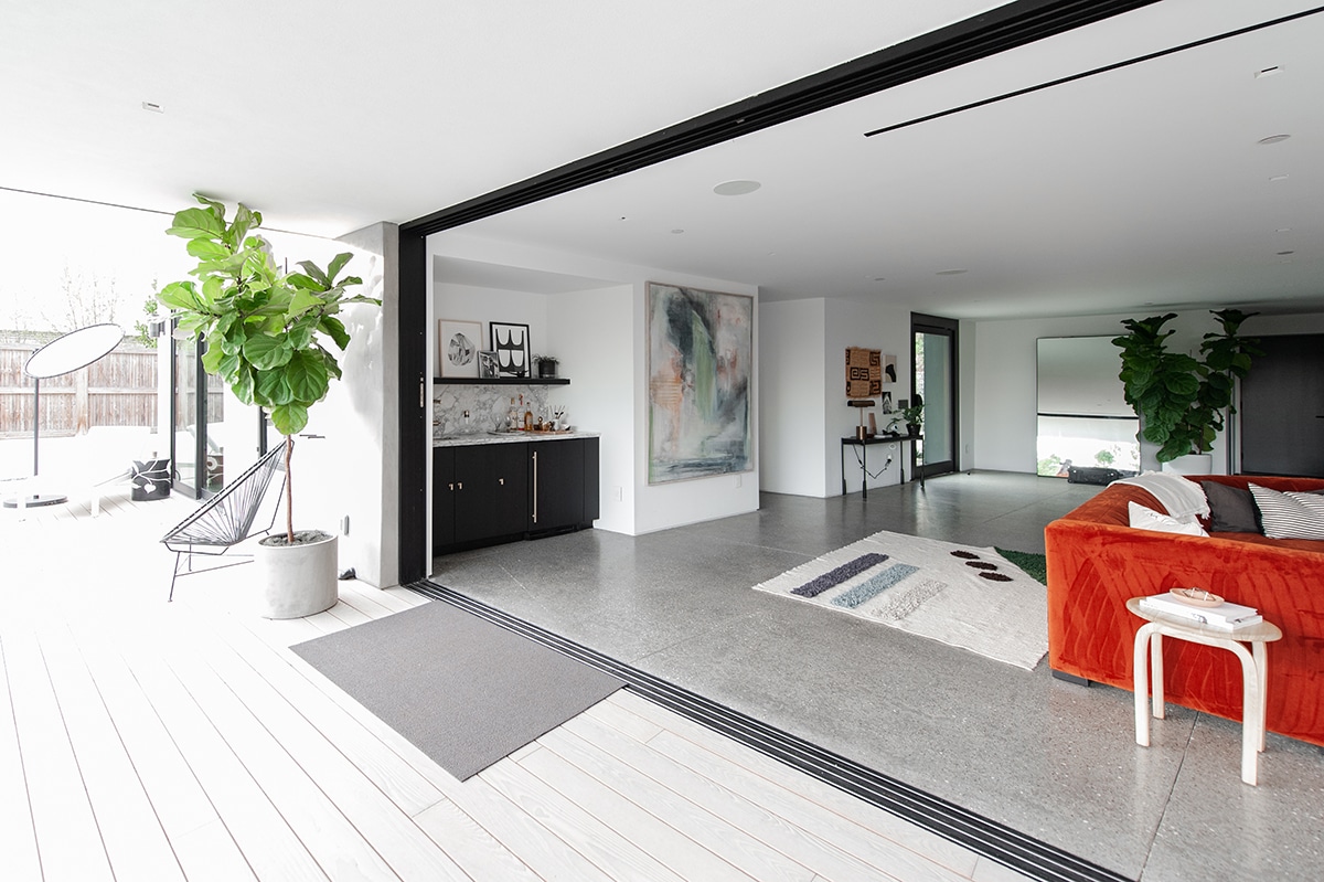 A living room with floor-to-ceiling, pocketing multi-slide doors open wide to the backyard patio.