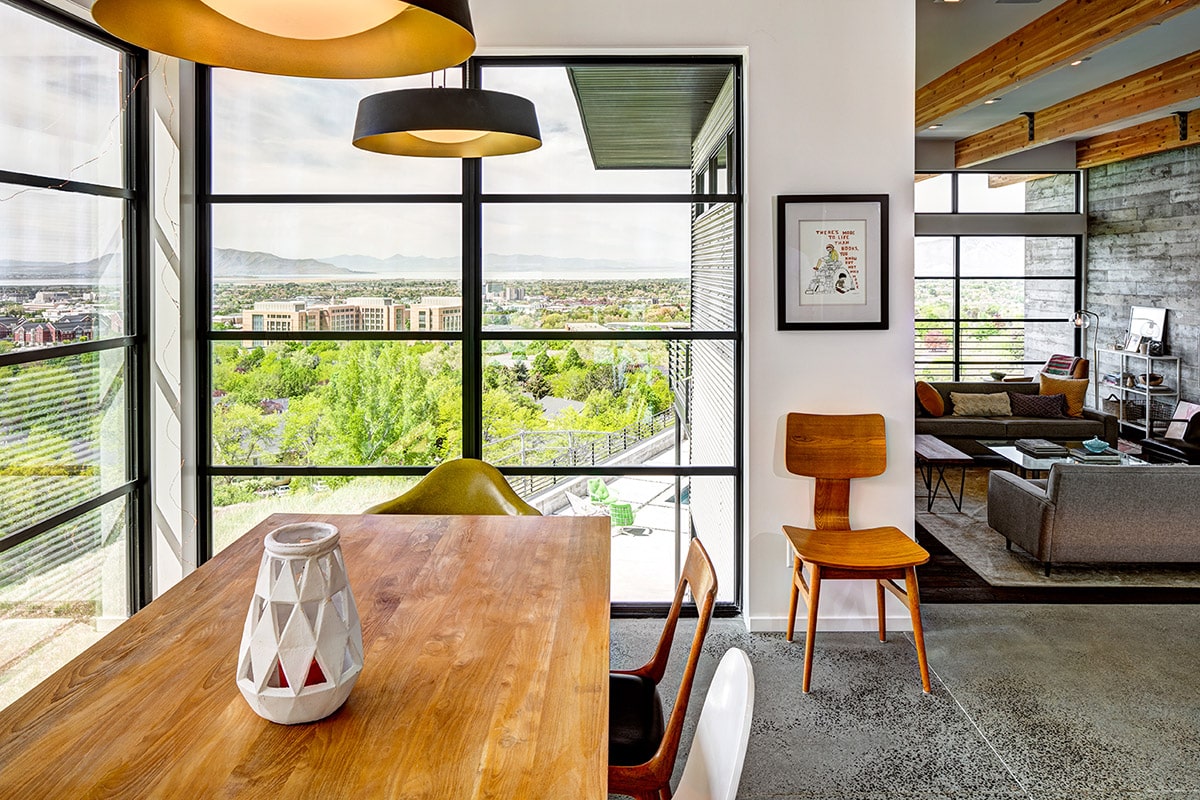 Large, divided lights fixed windows frame views of green landscape around a dining room table.