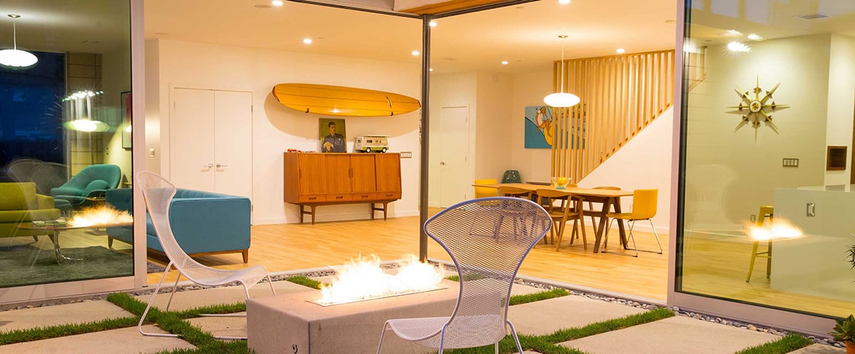 A large 90-degree multi-slide door opens to connect the interior space to the outdoor patio with a fireplace.