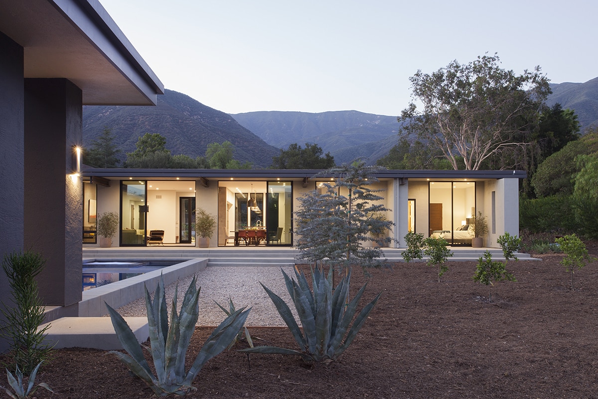 A view of the home’s façade with several open sliding glass doors connecting to the backyard.