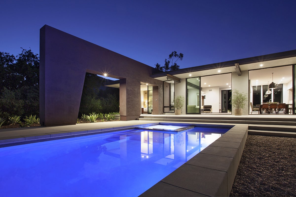 A home with a large pool opens up through sliding glass doors.