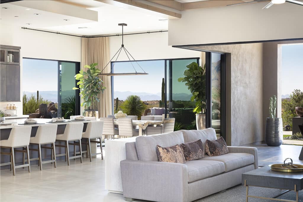 Multiple floor-to-ceiling sliding glass doors open to envelop the indoor living space with a seamless view of a mountain landscape.