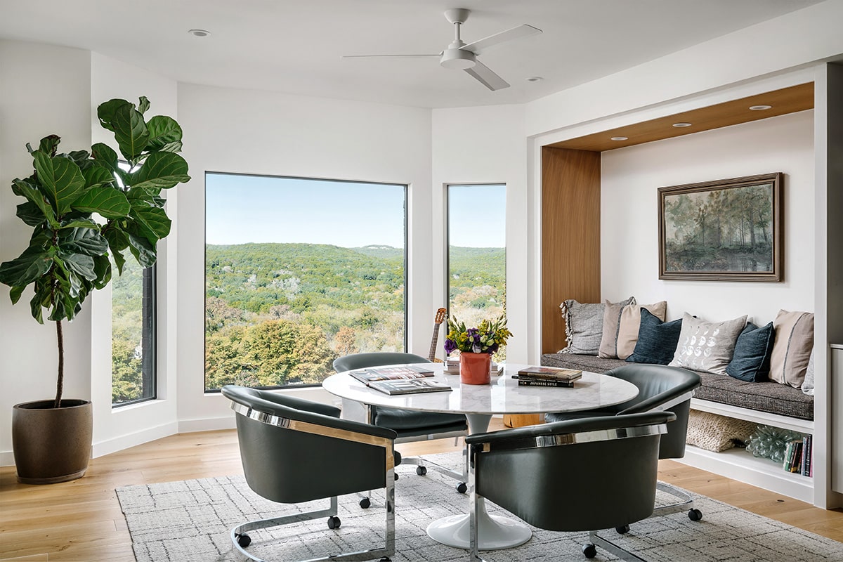 Natural daylight pours into a combined dining and den area through a picture window flanked by fenestration.