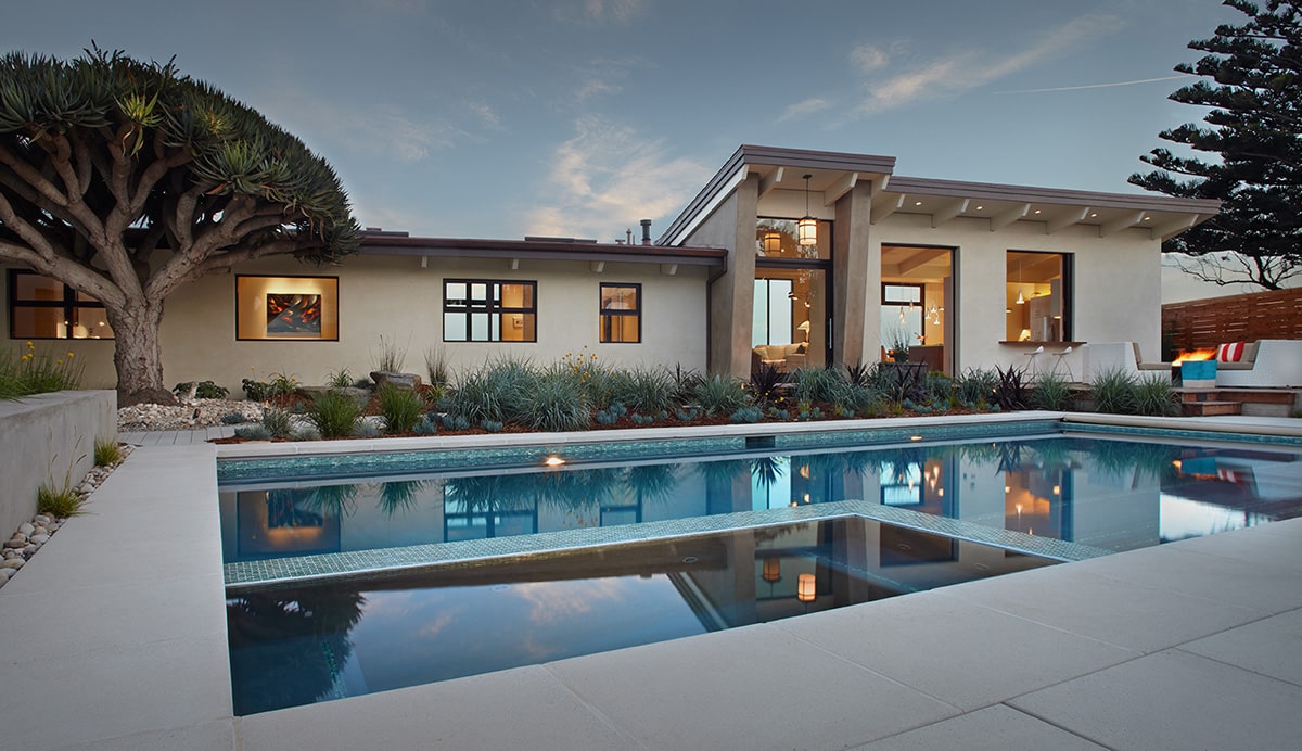 A view of the back of the home, dotted with windows and a large glass door, and a large swimming pool.