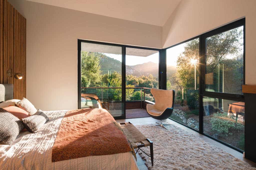 A sliding glass door that opens to a private balcony lets in natural light alongside large windows that make the corner of the bedroom nearly all glazing.