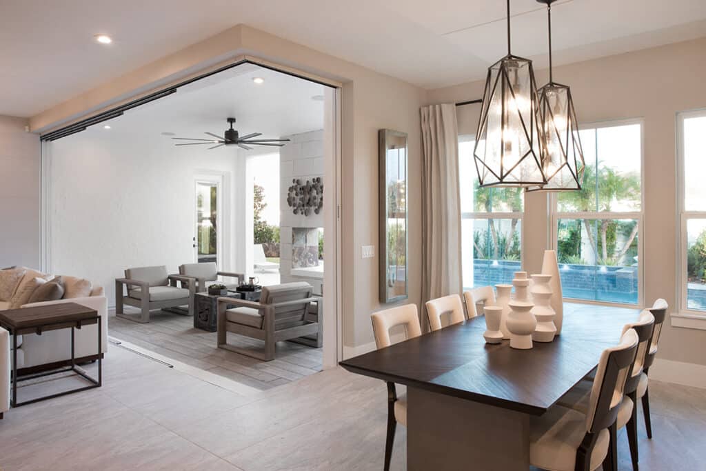 An outdoor seating area seamlessly transitions to a dining room through a fully opened 90-degree multi-slide glass door.