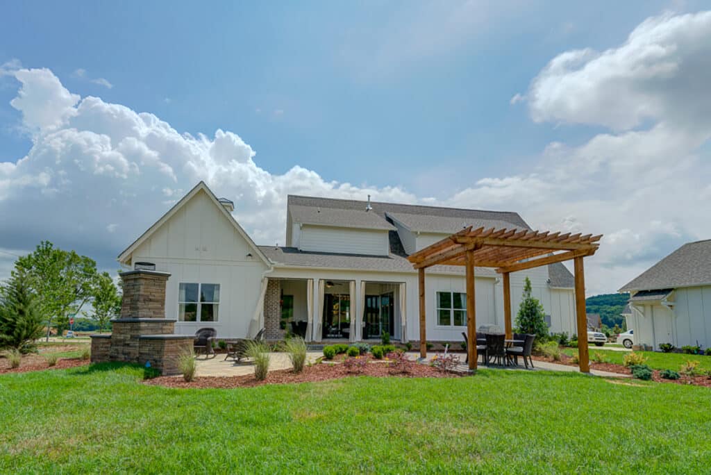 A lush backyard with green grass and a tall pergola is connected to the back of a house with multi-slide glass doors.