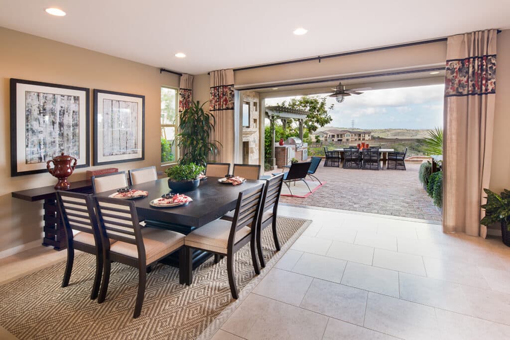 An indoor dining area is connected to an outdoor seating area via pocketed multi-slide glass doors.