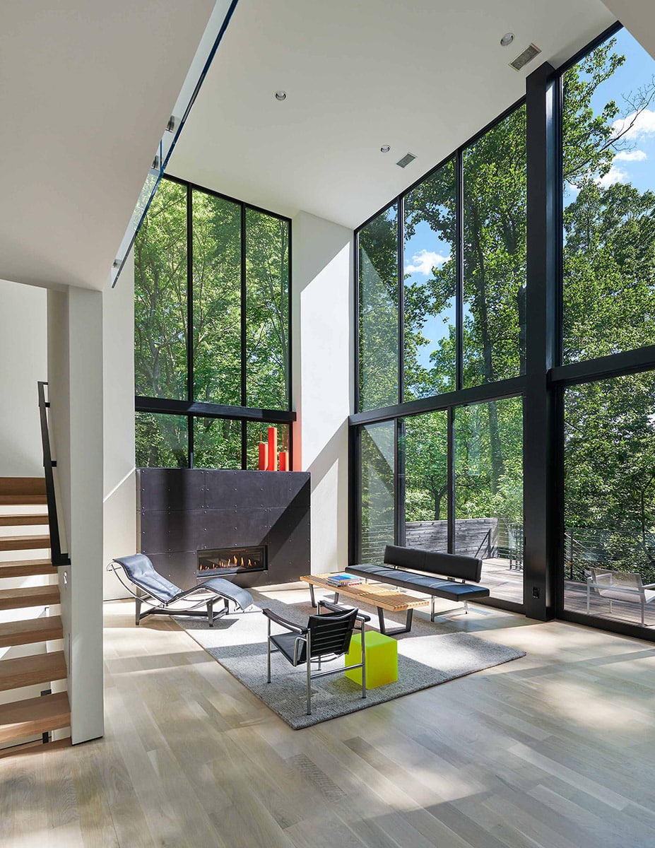 A serene environment is created in interior living spaces through walls of glass that let in natural light and views of green landscape.