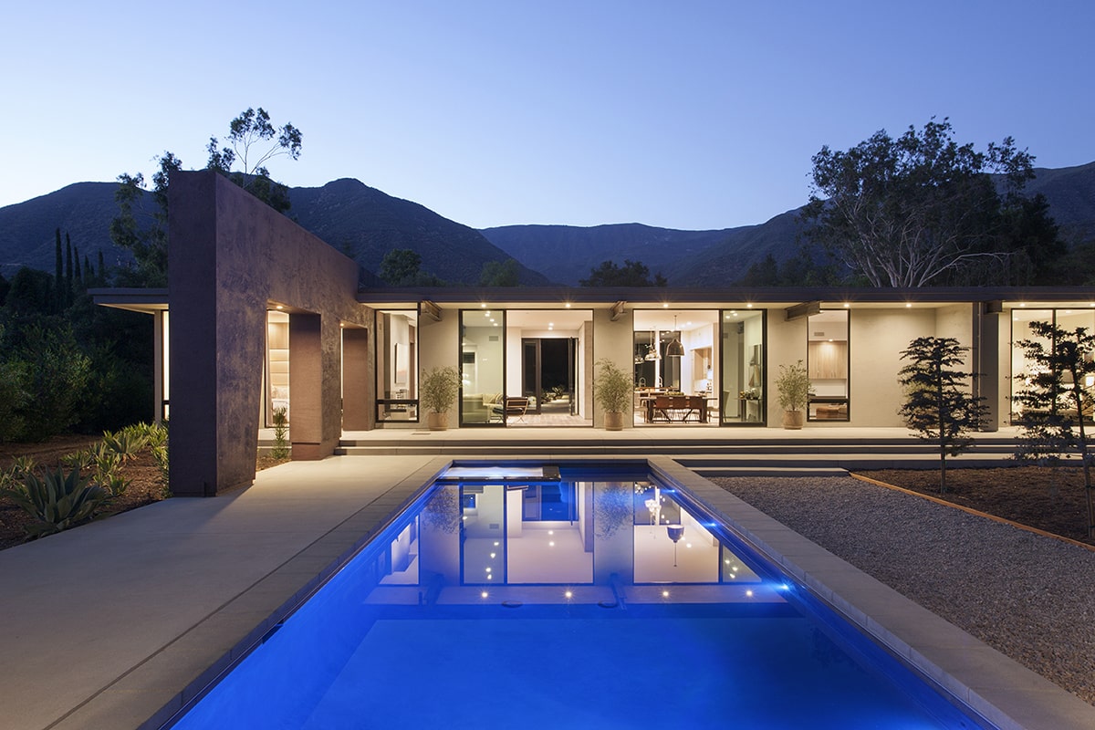 A nighttime view from the pool of the open, multi-slide doors connecting the living room, dining room, and master suite to the backyard.