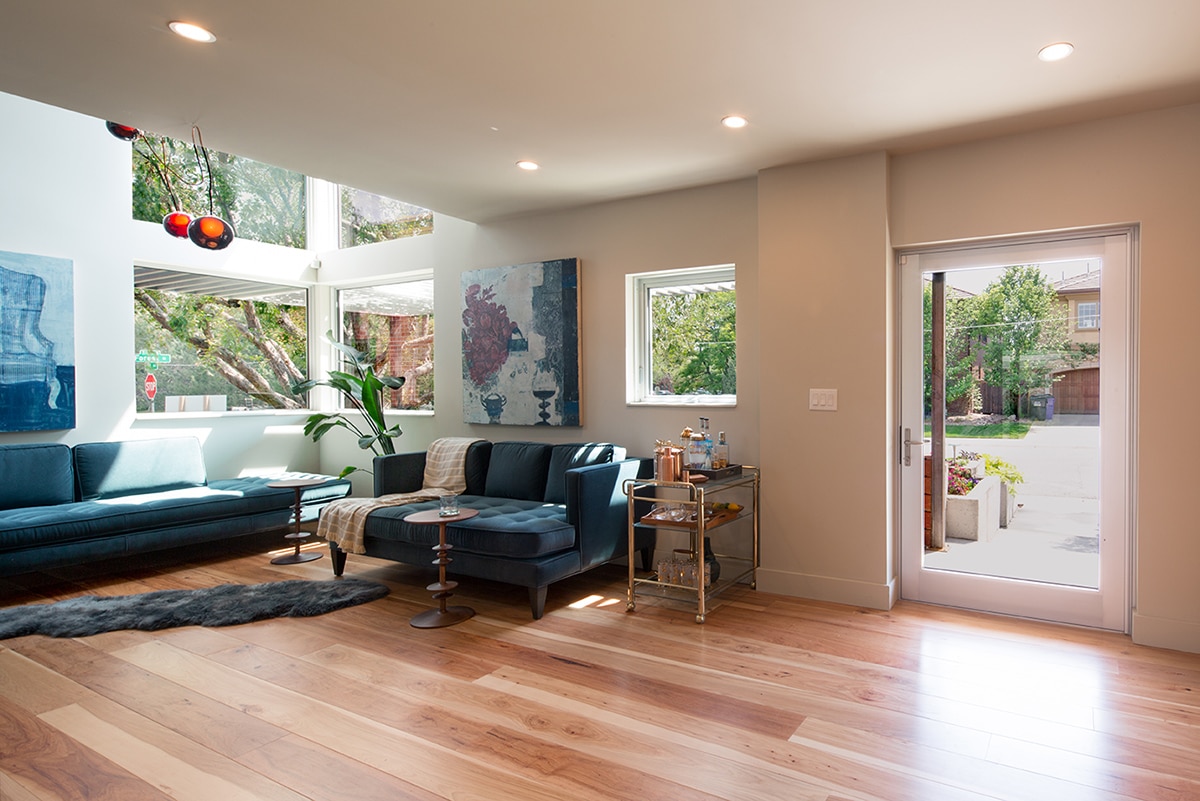 A large, hinged door and several windows allow bright sunlight into the living room.