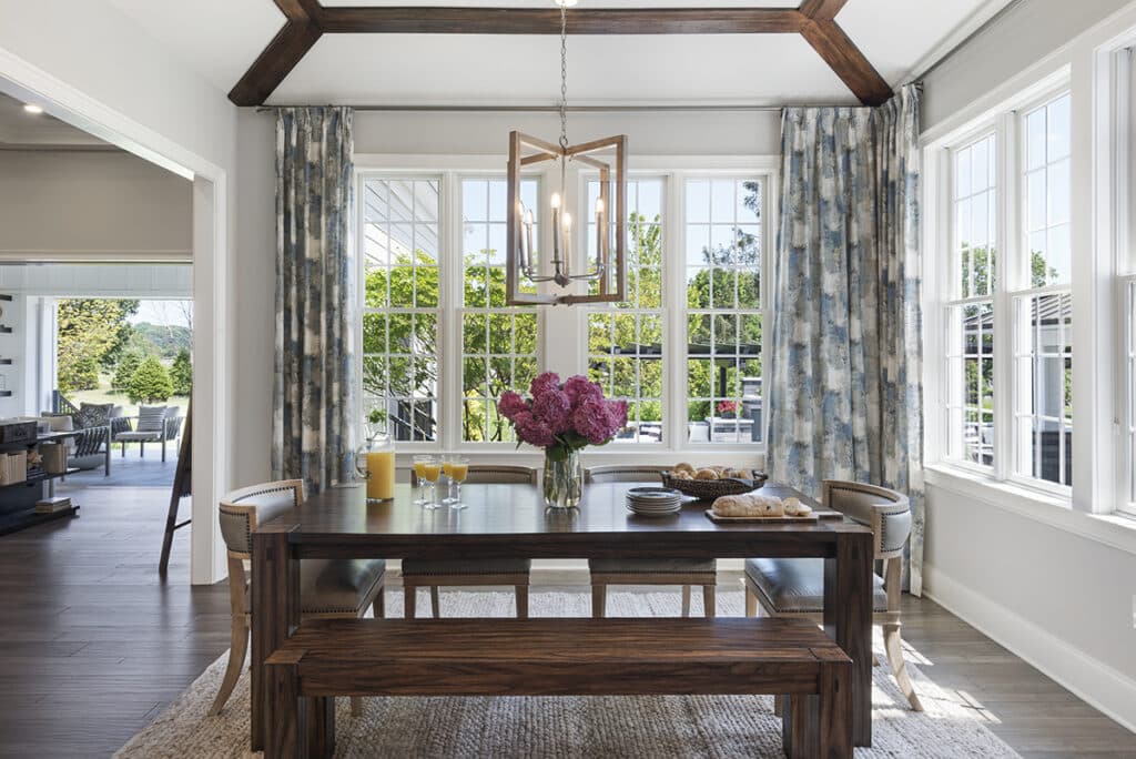 A glassy breakfast nook is bathed in sunlight coming from an open multi-slide glass door and surrounding windows.