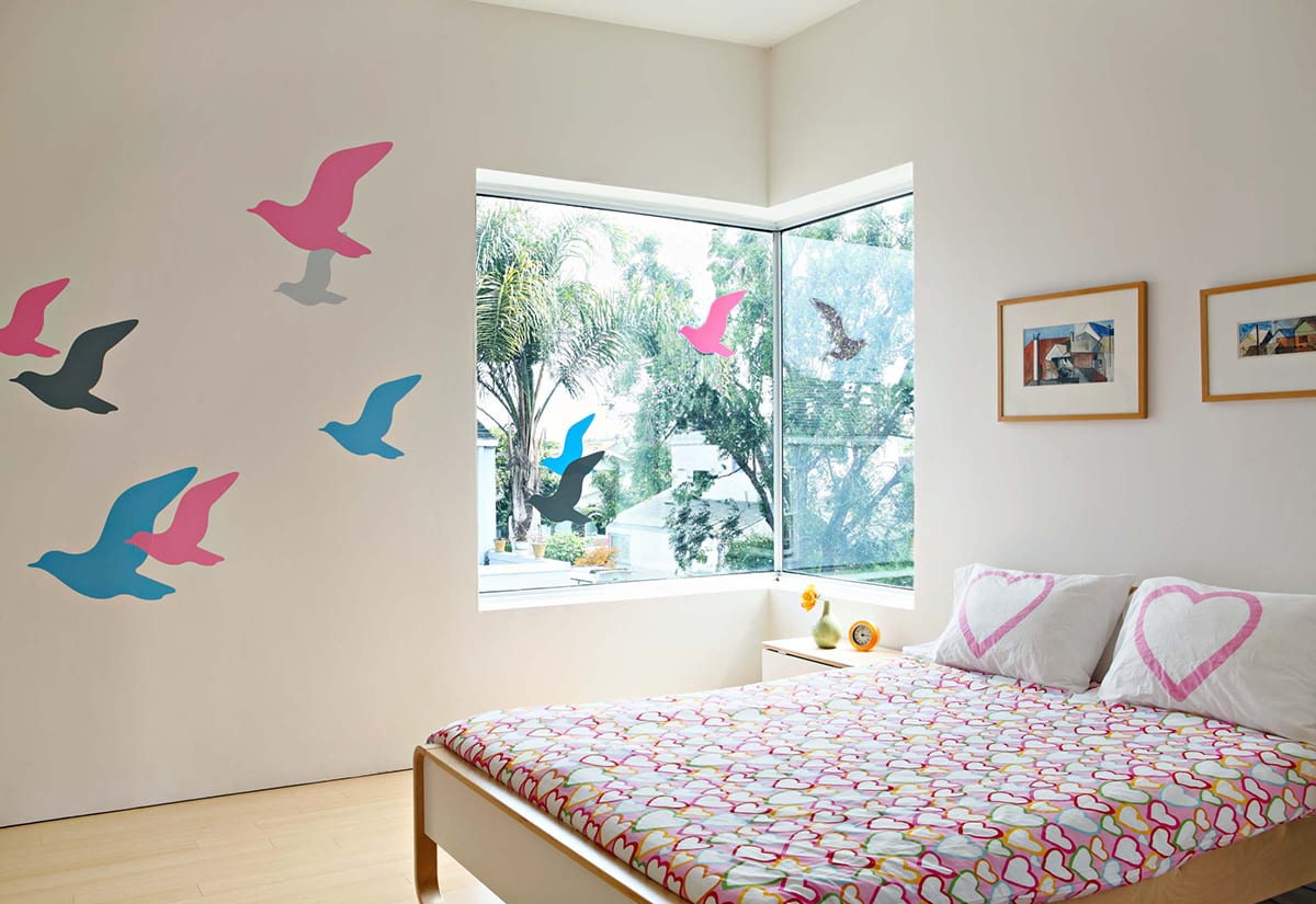 A corner window covered with bird decals bathes a bedroom with copious amounts of Southern California sunshine.
