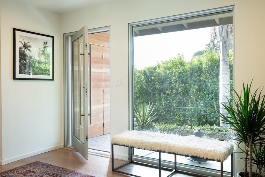 04-180907_6d_0090_lrpslr_180919final-MOD An aluminum pivot door next to a large, fixed window look out to a lush front yard.