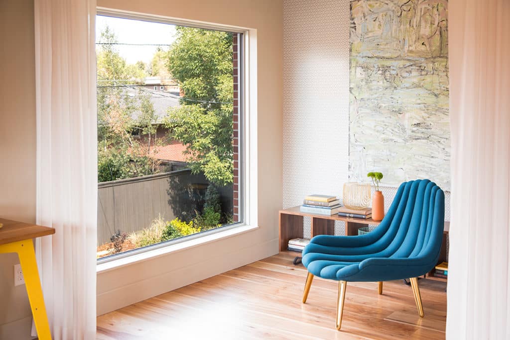 An oversized window helps light a corner of the room with a short bookshelf and blue chair.