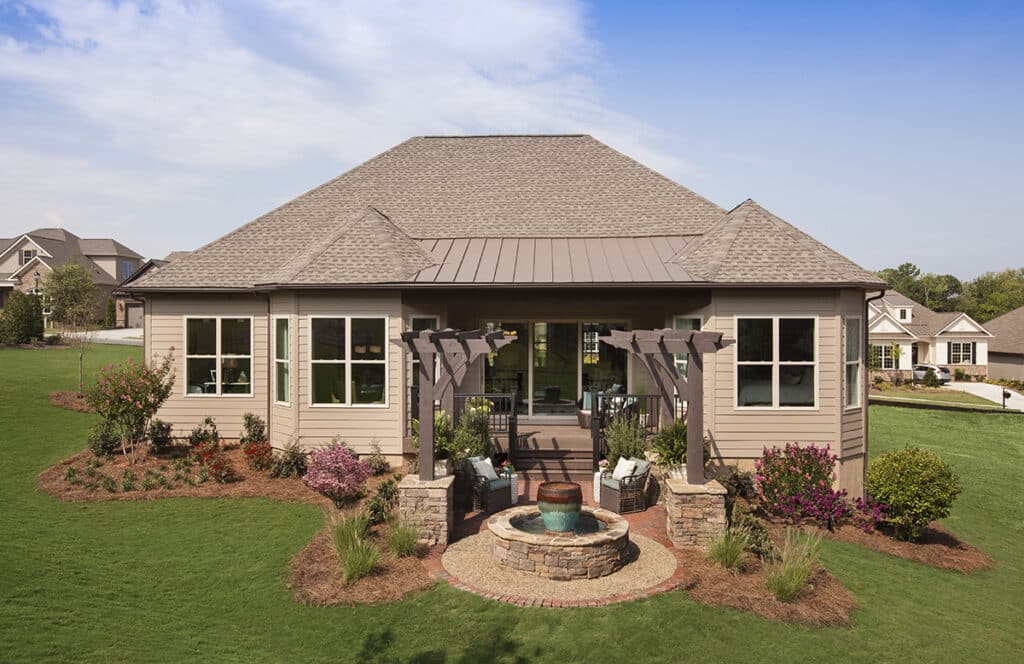 The back of a house with tan paneling and a multi-slide glass door that transitions to a shaded outdoor seating area.