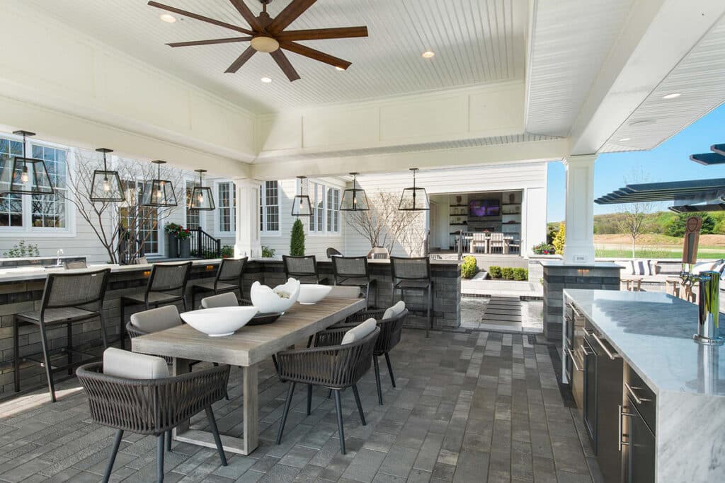 A covered outdoor dining area seamlessly connects to the interior of the house through an open multi-slide glass door.