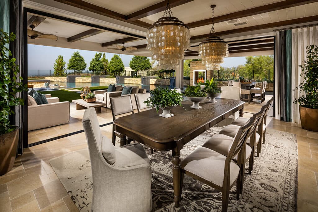 Floor-to-ceiling moving glass walls that meet at a 90-degree post less corner connect an indoor dining room to an outdoor living space.