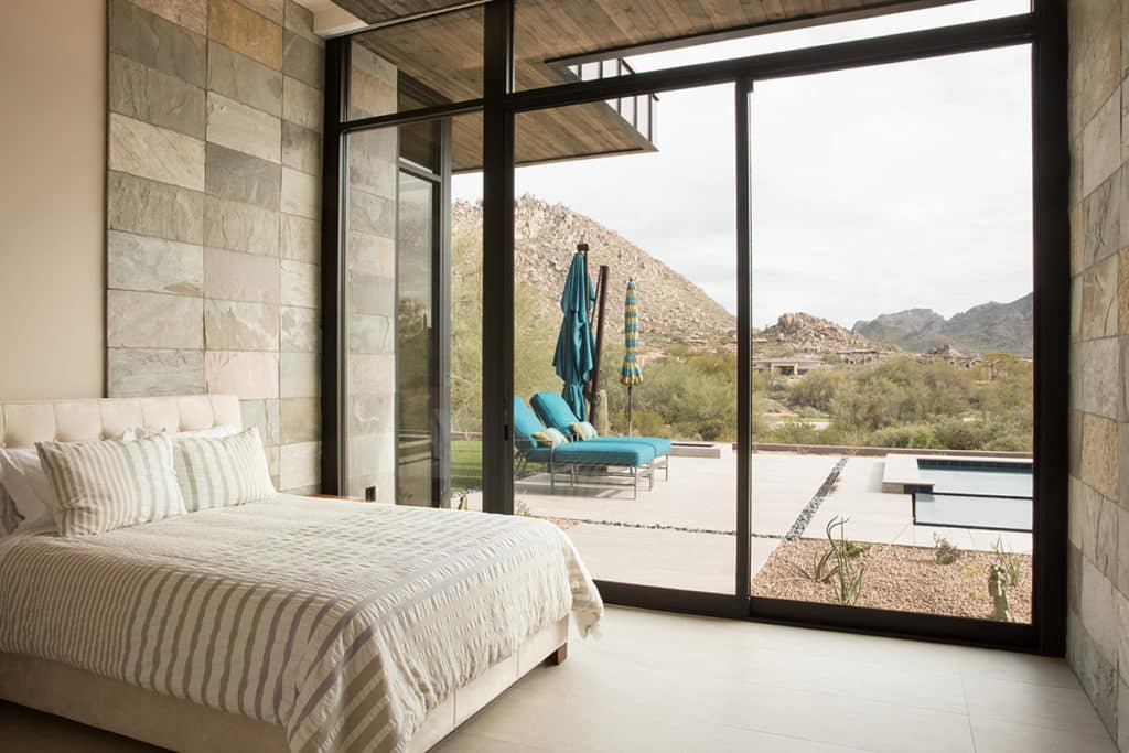 Every room in the house has a view through massive glass, like this bedroom that has views of the backyard and mountains beyond.