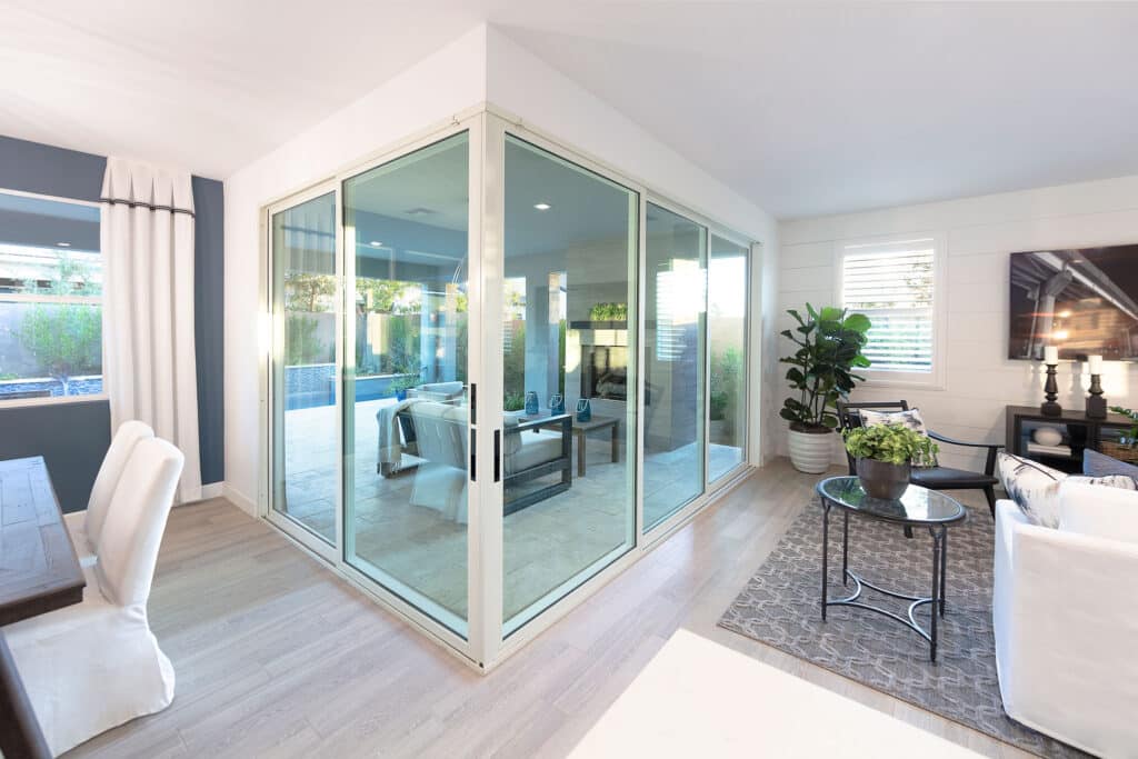 A closed 90-degree multi-slide glass door separates the outdoor living space and pool from the indoor living and dining room.