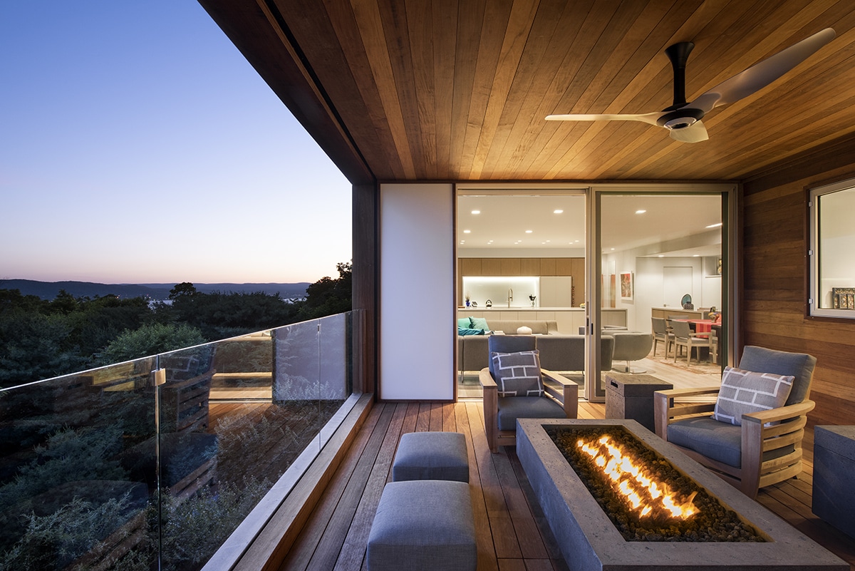 A floor-to-ceiling sliding glass door connects the living room to the deck seating area with a fireplace.