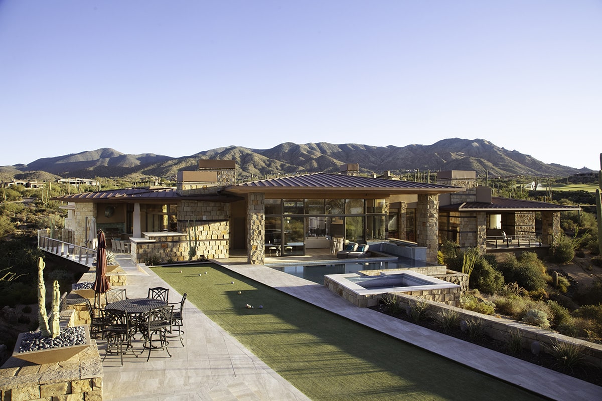 12-foot-wide sliding glass doors in a window wall open onto a spacious backyard featuring a geometric pool and bocce ball court.