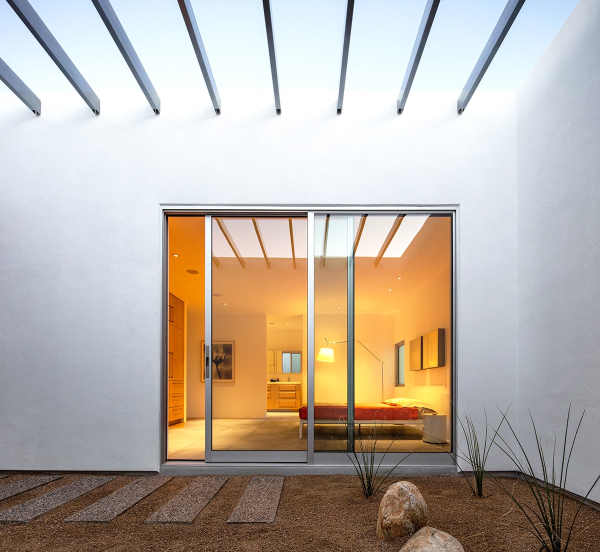 A tall sliding glass door connects the master bedroom to an outdoor courtyard with views of the sky.