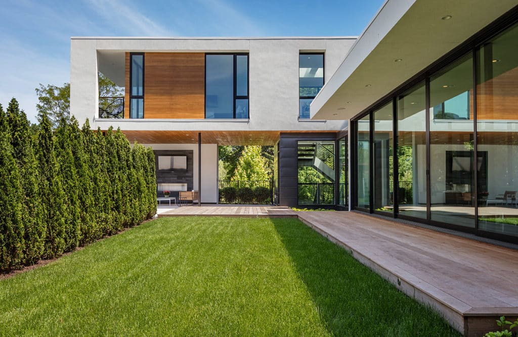 A view of the home’s glazing facing a grassy lawn with shrub trees.