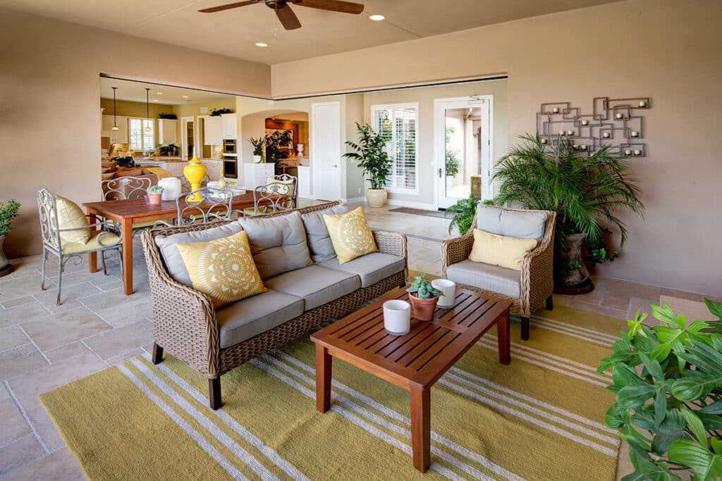 A covered patio hosts an outdoor living space surrounded by an open 90-degree multi-slide glass door that leads indoors.