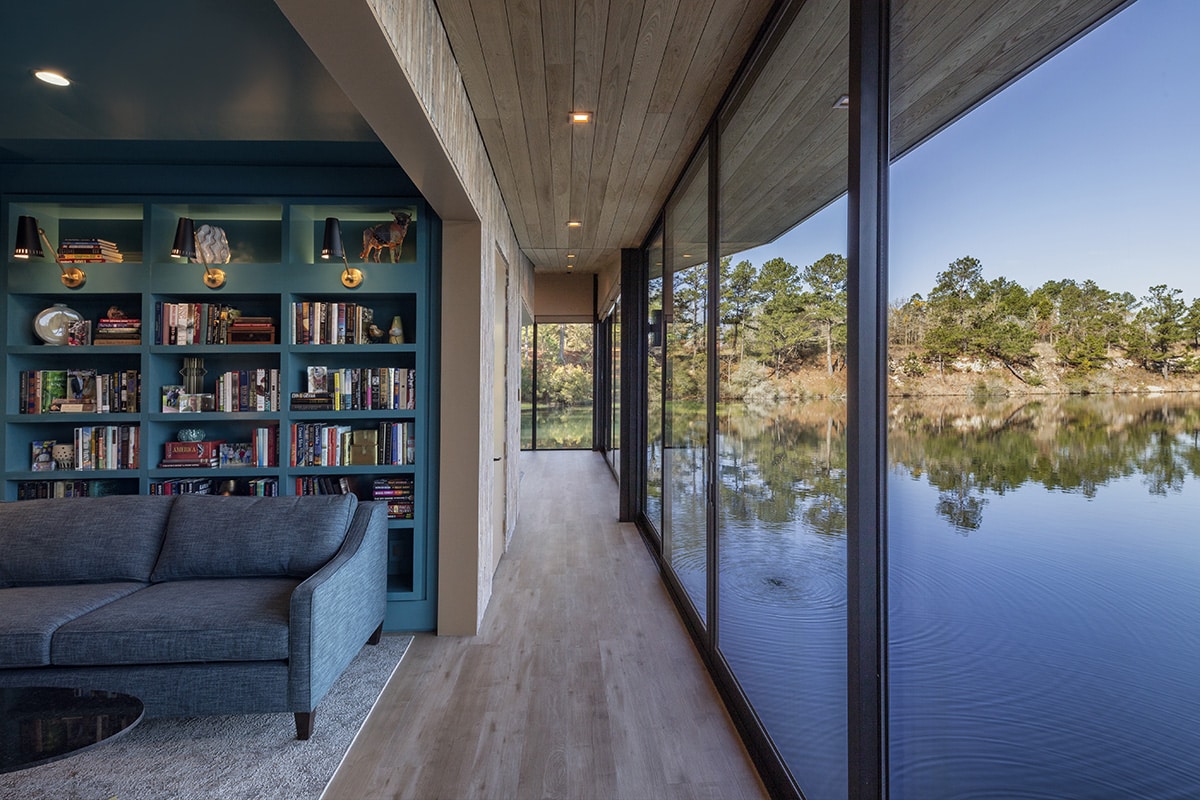 A vibrant library shares a long glass wall with the hallway, with the lake visible outside.