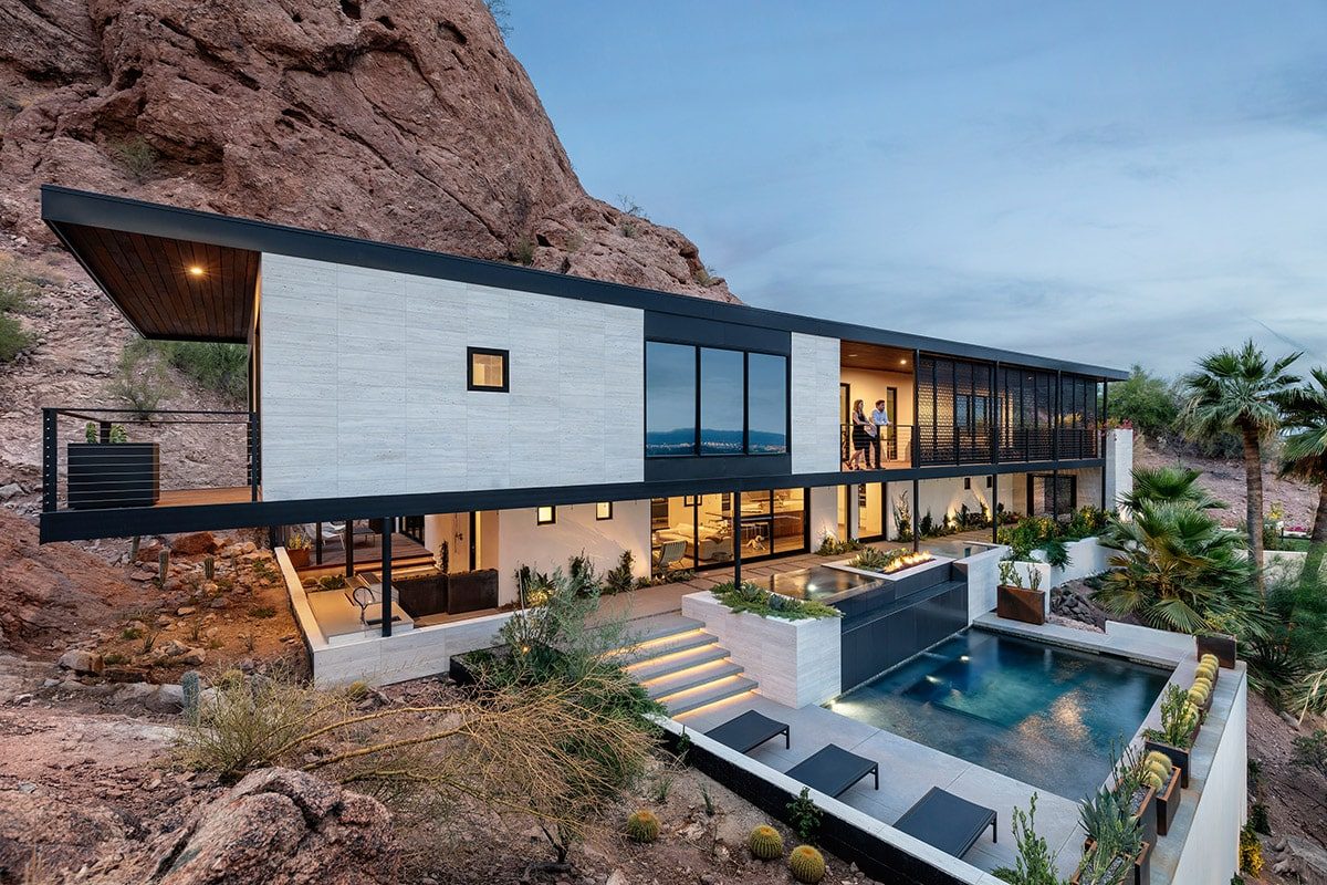 06-RR-1852-web A two-story house built into a mountain side displays a number of floor-to-ceiling window walls and multi-slides looking out onto a pool.