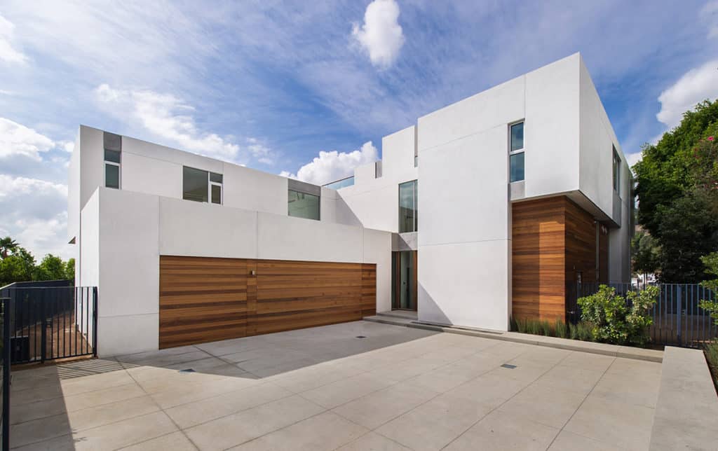 A front view of the nearly all white home with wood paneling and windows of various sizes.